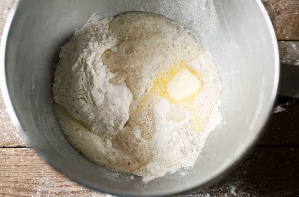 Hands kneading soft garlic naan dough in a steel mixing bowl