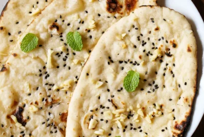 Stack of soft garlic naan brushed with garlic butter and cilantro on a wooden board