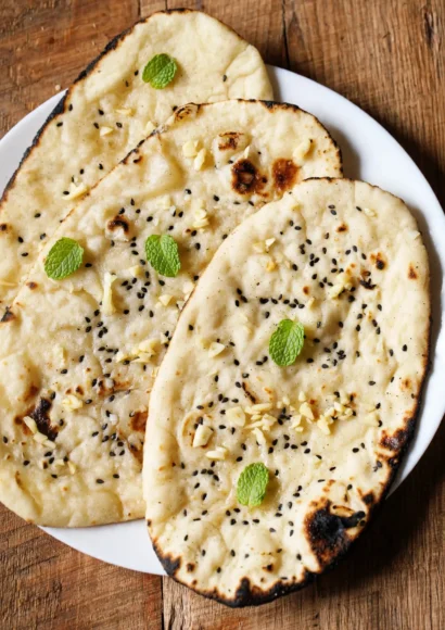 Stack of soft garlic naan brushed with garlic butter and cilantro on a wooden board