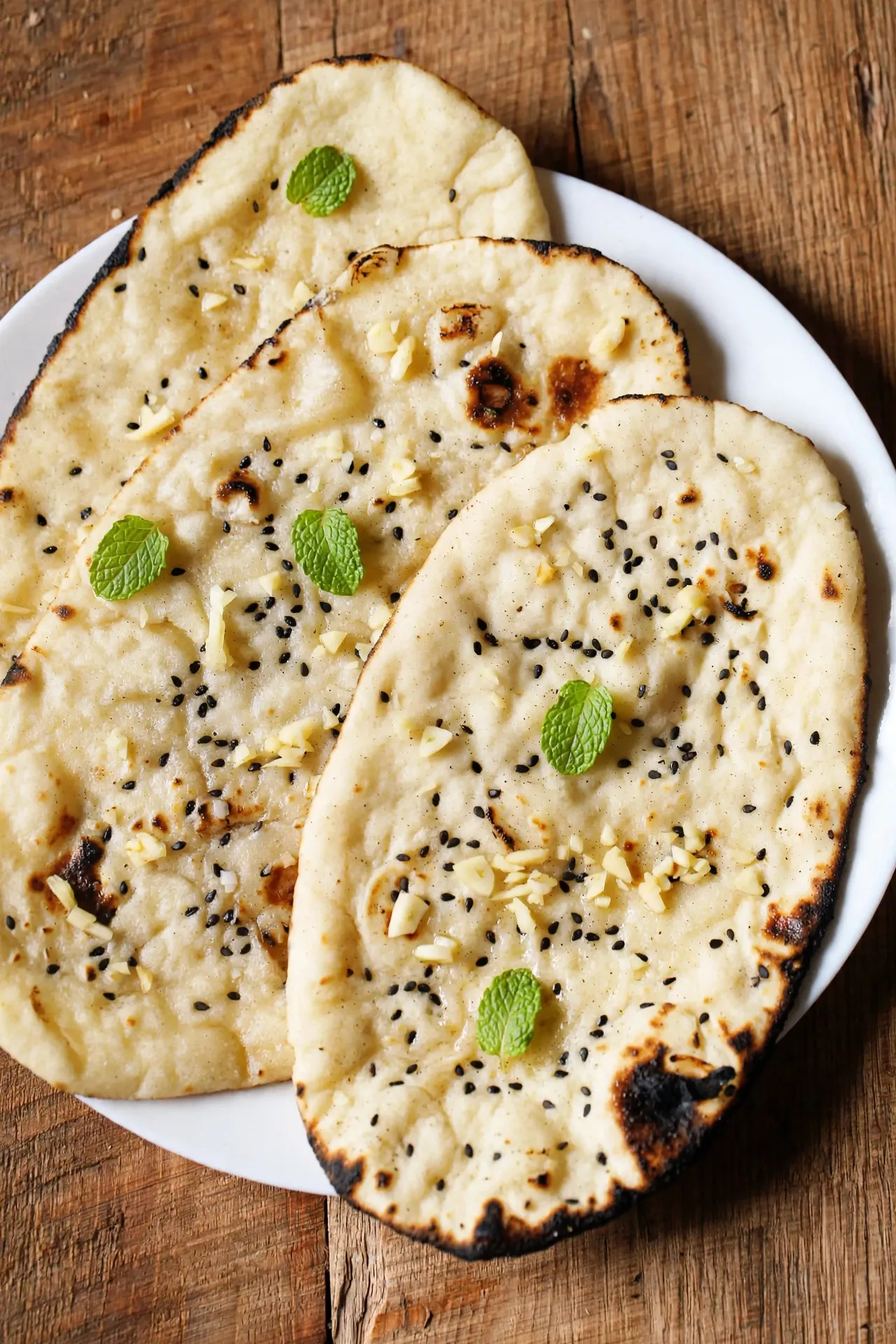 garlic-naan-recipe-hero » Tavolart Stack of soft garlic naan brushed with garlic butter and cilantro on a wooden board
