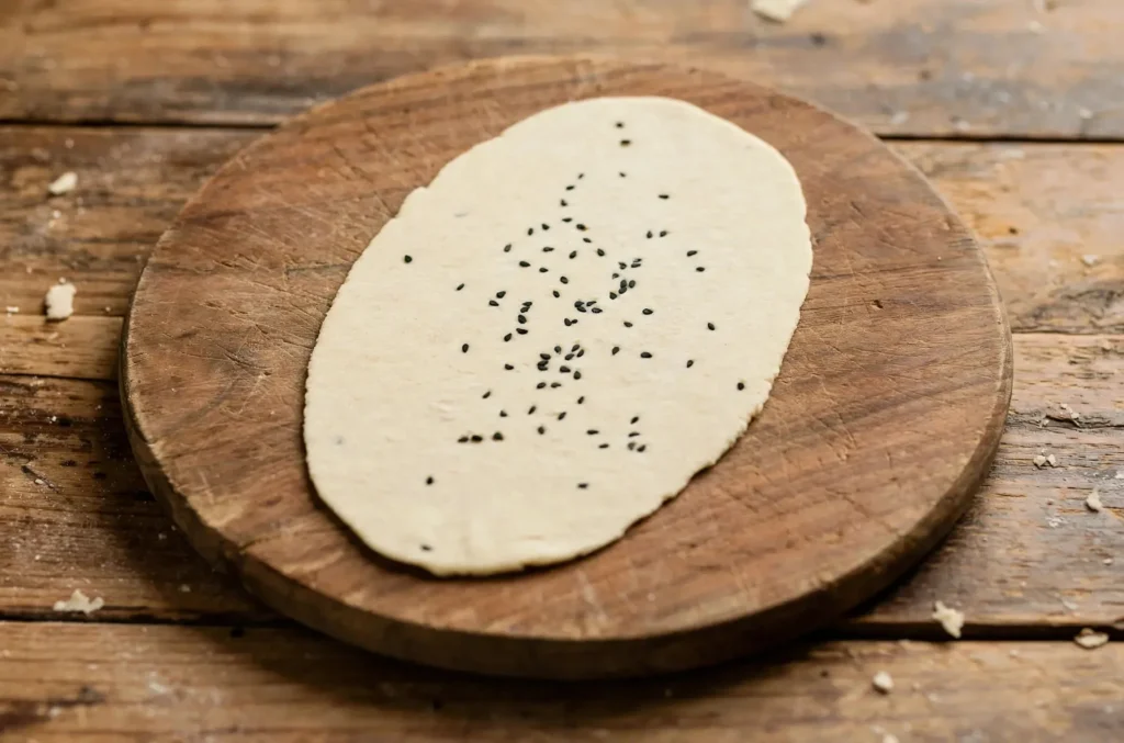 Rolling garlic naan dough into an oval shape on a floured board